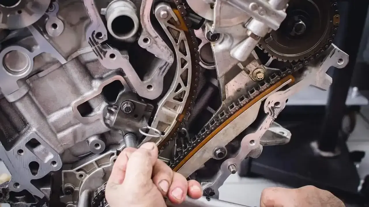 Mechanik dokręca śrubę przy rozrządzie silnika. Widać fragmenty łańcucha rozrządu i metalowe elementy, które mogą być częścią poduszki silnika.