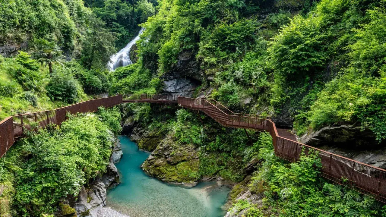 Sentiero panoramico tra gole e cascate, un esempio di posti strani da visitare in Italia, con passerelle in metallo che si snodano tra la vegetazione lussureggiante.
