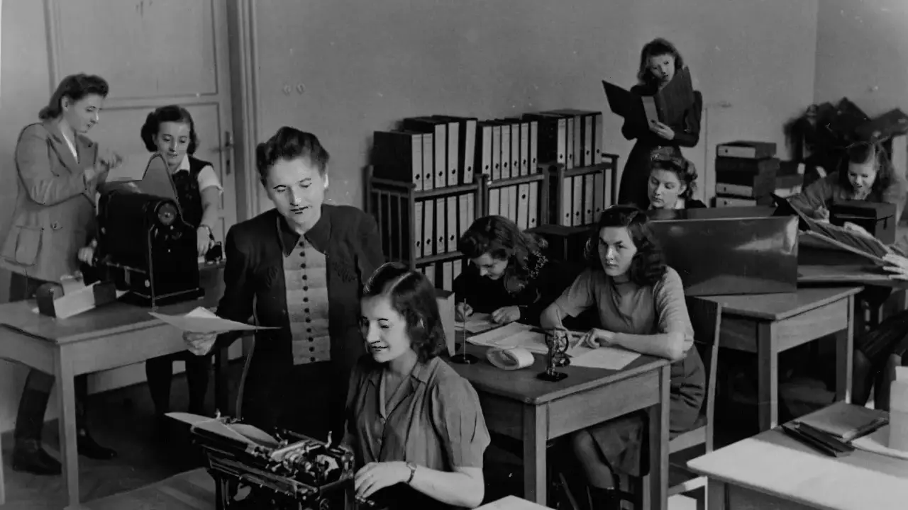 Kobiety pracujące w biurze, jedna przy maszynie do pisania, inne nad dokumentami. To właśnie tajne komplety, czyli tajne nauczanie, które odbywało się w ukryciu.