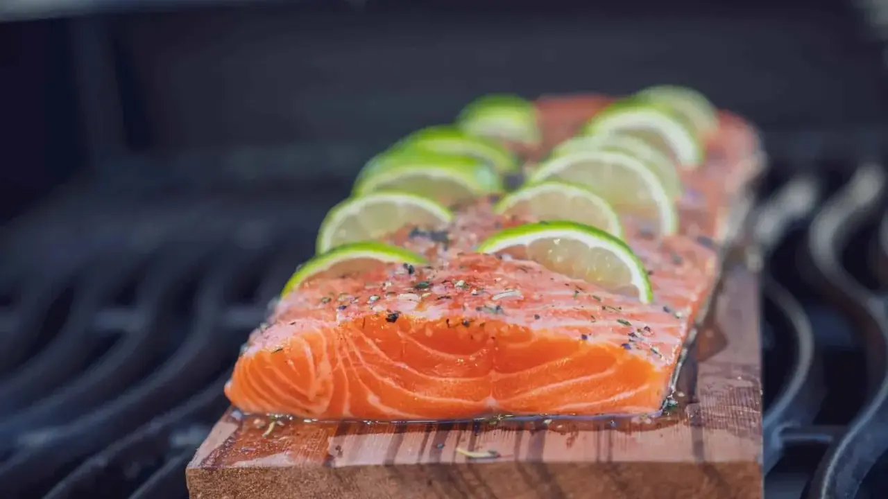 Lachs auf Zedernholz grillen, mit Limettenscheiben und Kräutern belegt. Ein saftiges Stück Fisch auf dem Rost.