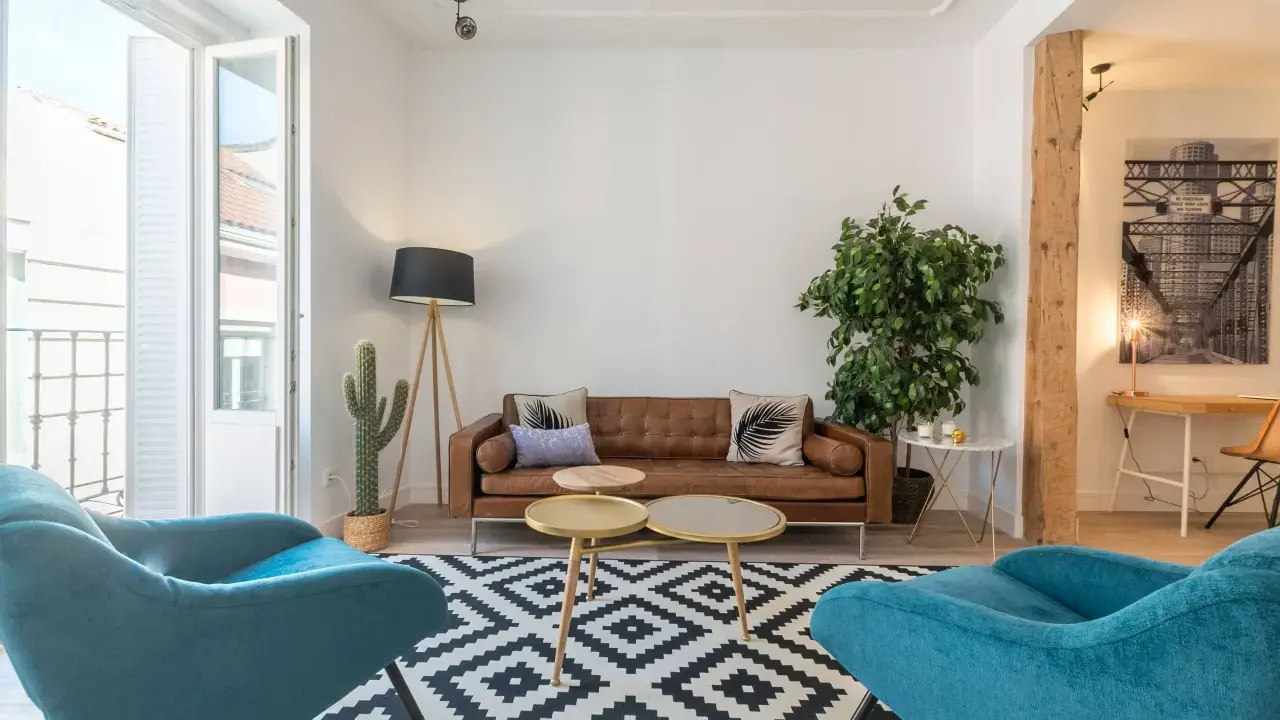 Brun soffa, turkosa fåtöljer och en stor kaktus ger en känsla av inredning 80-tal. Mönstrat golv och trädetaljer.