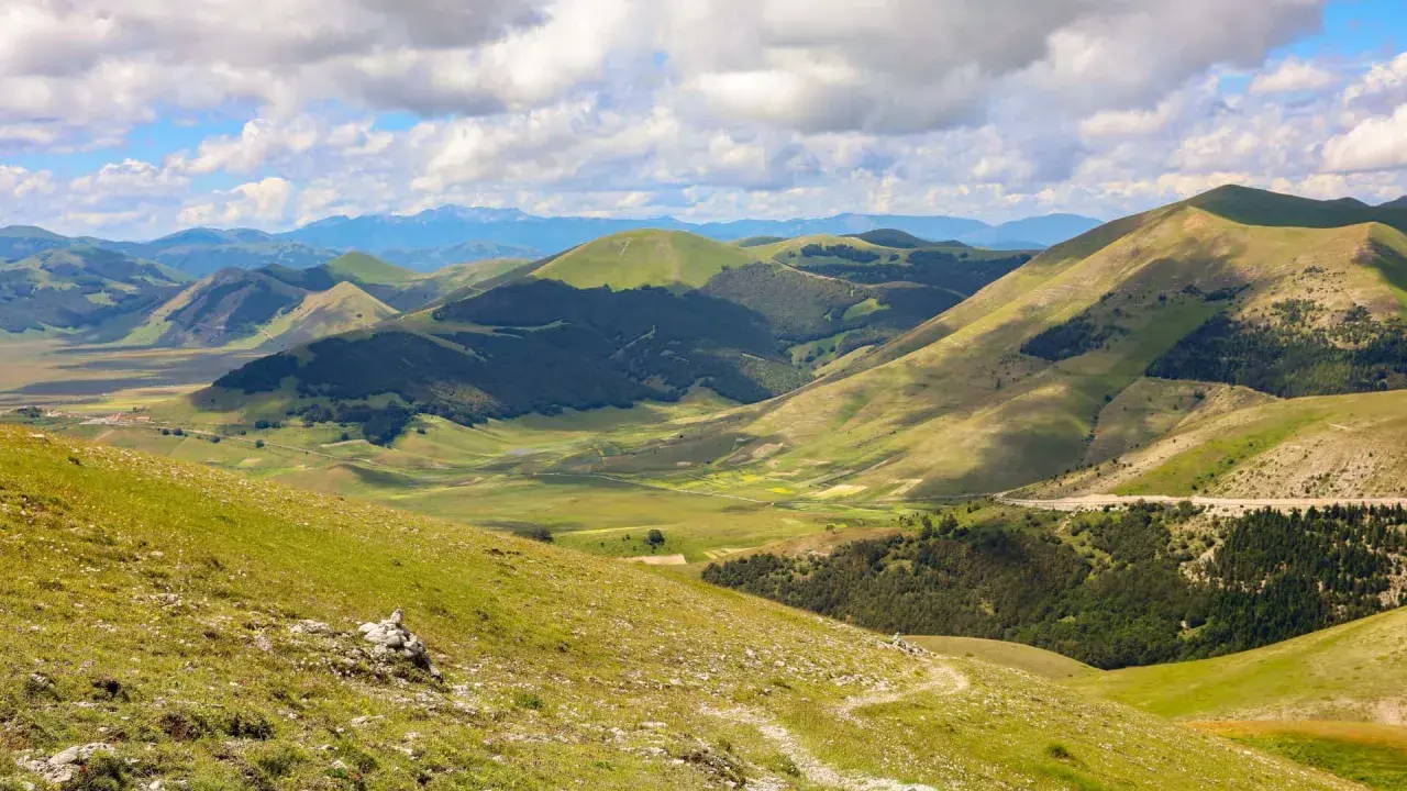 Panoramica dei Monti Sibillini, un paesaggio verdeggiante con dolci colline e valli, ideale per scoprire cosa vedere in questa zona.