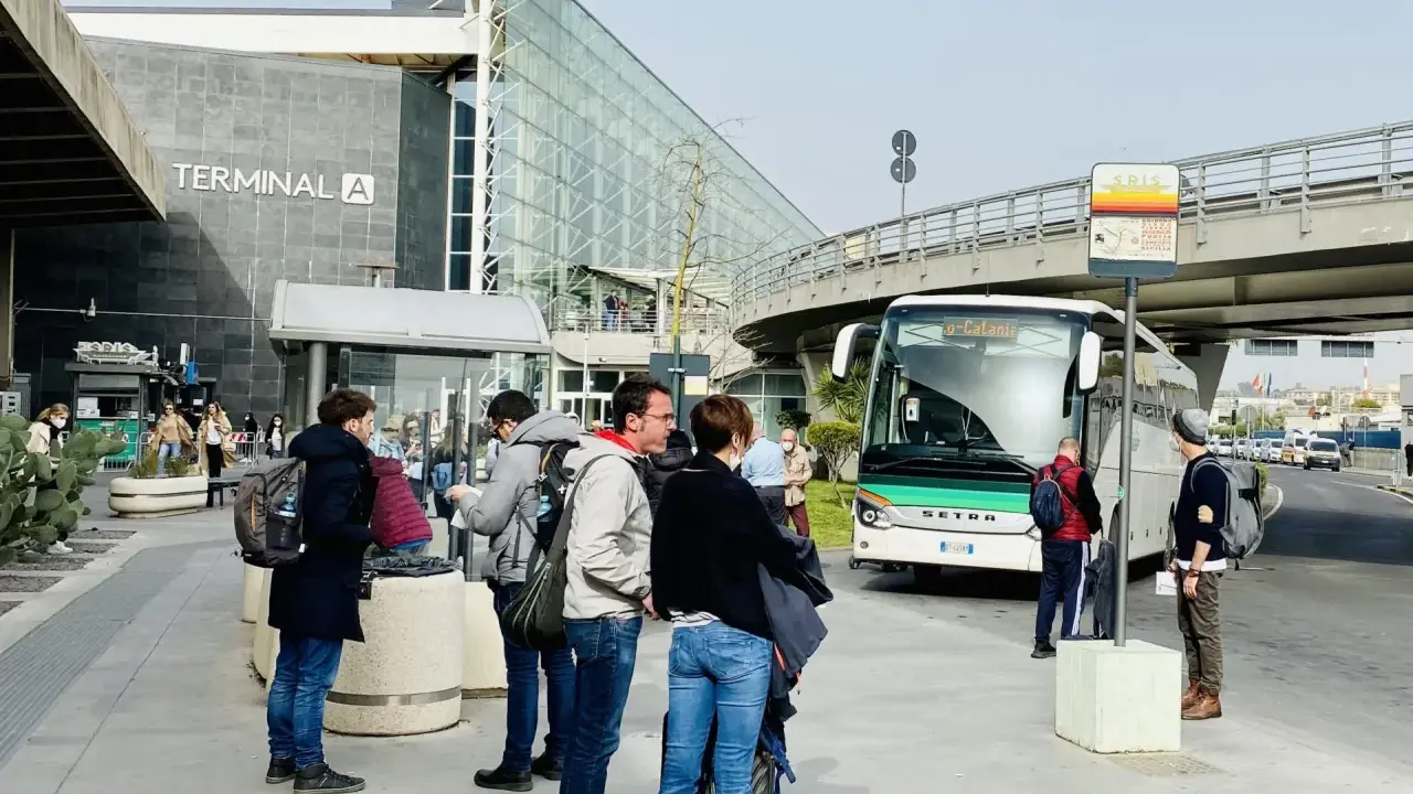 Ludzie czekają na autobus przed Terminalem A na lotnisku w Katanii.