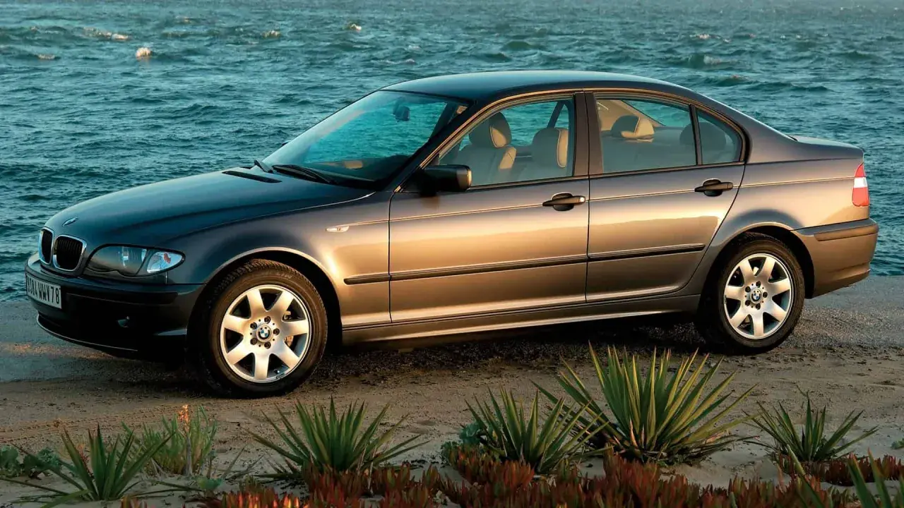 Szary sedan BMW E4 na plaży, z morzem w tle.