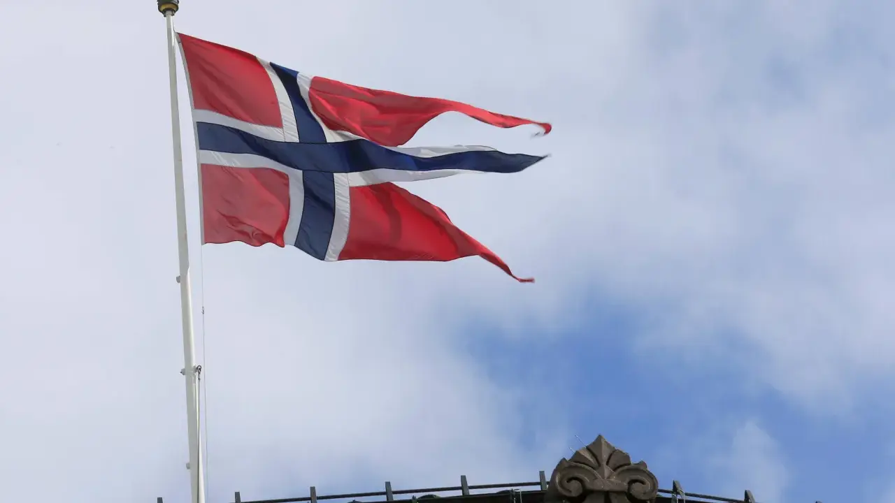 Norwegische Flagge weht im Wind über einem Gebäude. Die Diskussion über den Stromverbrauch in Norwegen ist aktuell.