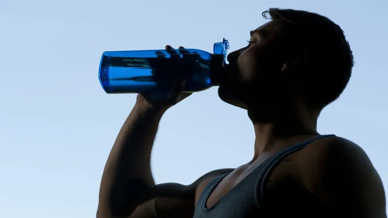 Mann trinkt aus blauer Flasche, erfrischt sich nach dem Sport.