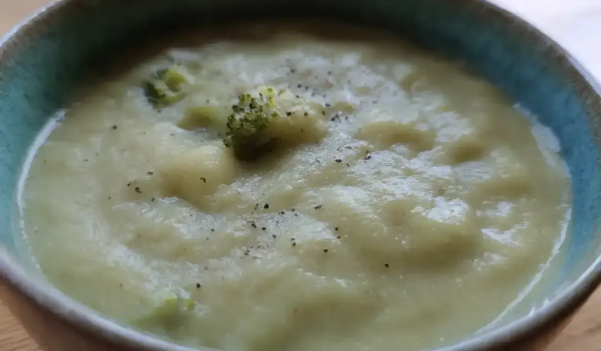 En krämig potatis och broccolisoppa, toppad med lite svartpeppar, serveras i en blå kantad skål.