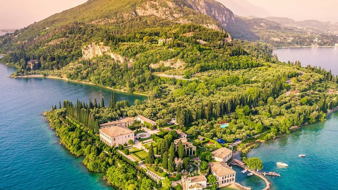 Punta San Vigilio: eine Villa mit Gärten und Zypressen am türkisfarbenen Gardasee, umgeben von grünen Hügeln.