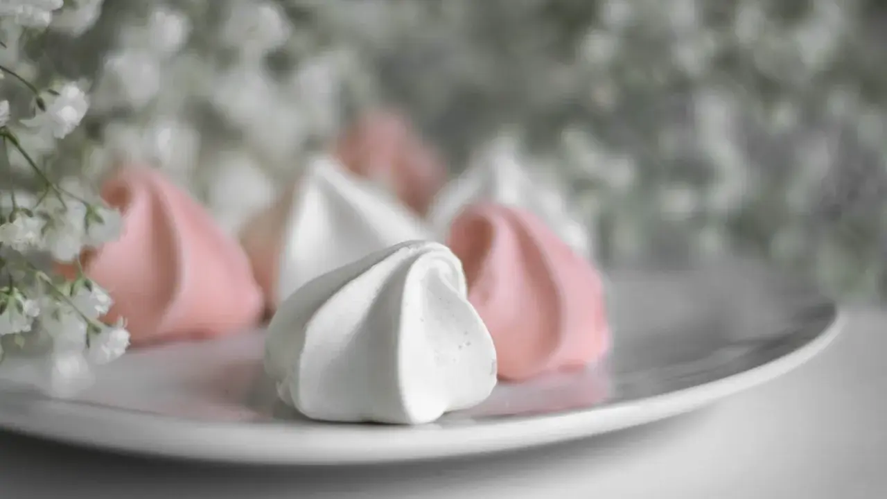 Douceur aérienne de meringue italienne rose et blanche sur une assiette, avec des petites fleurs en arrière-plan.
