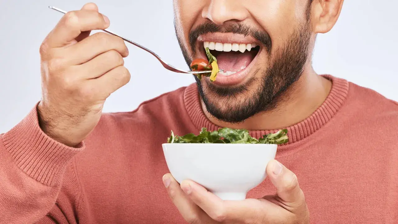 Mann isst Salat, achtet auf die richtige Anzahl, wie oft kauen, für eine gute Verdauung.