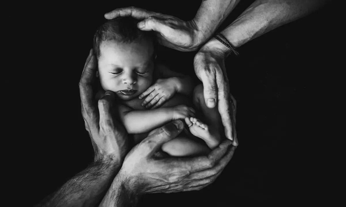 Mani adulte proteggono un neonato addormentato, simbolo di amore e cura. Un futuro di bilinguismo bambini inizia qui.