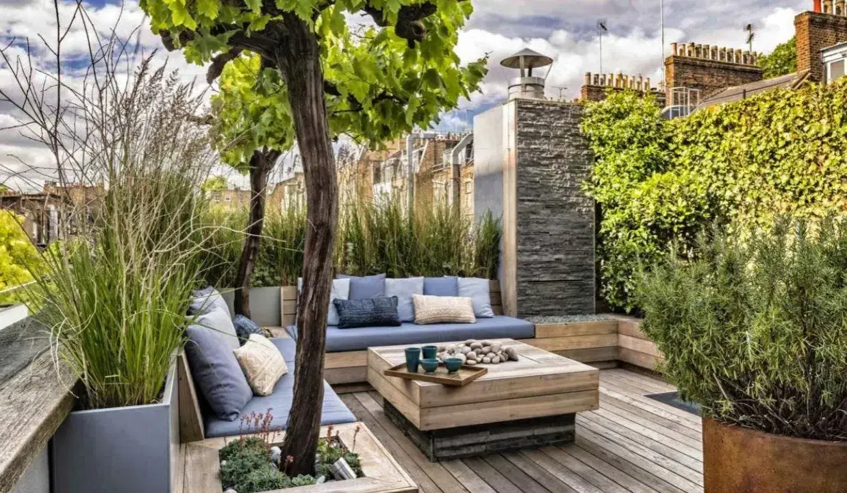Un coin salon confortable pour aménager une terrasse avec des coussins bleus, une table basse en bois et une végétation luxuriante.