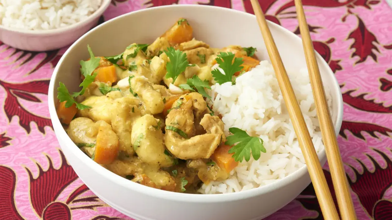 Ein köstliches Bananencurry mit Hähnchen, Karotten und Reis, garniert mit Koriander. Chopsticks liegen bereit.