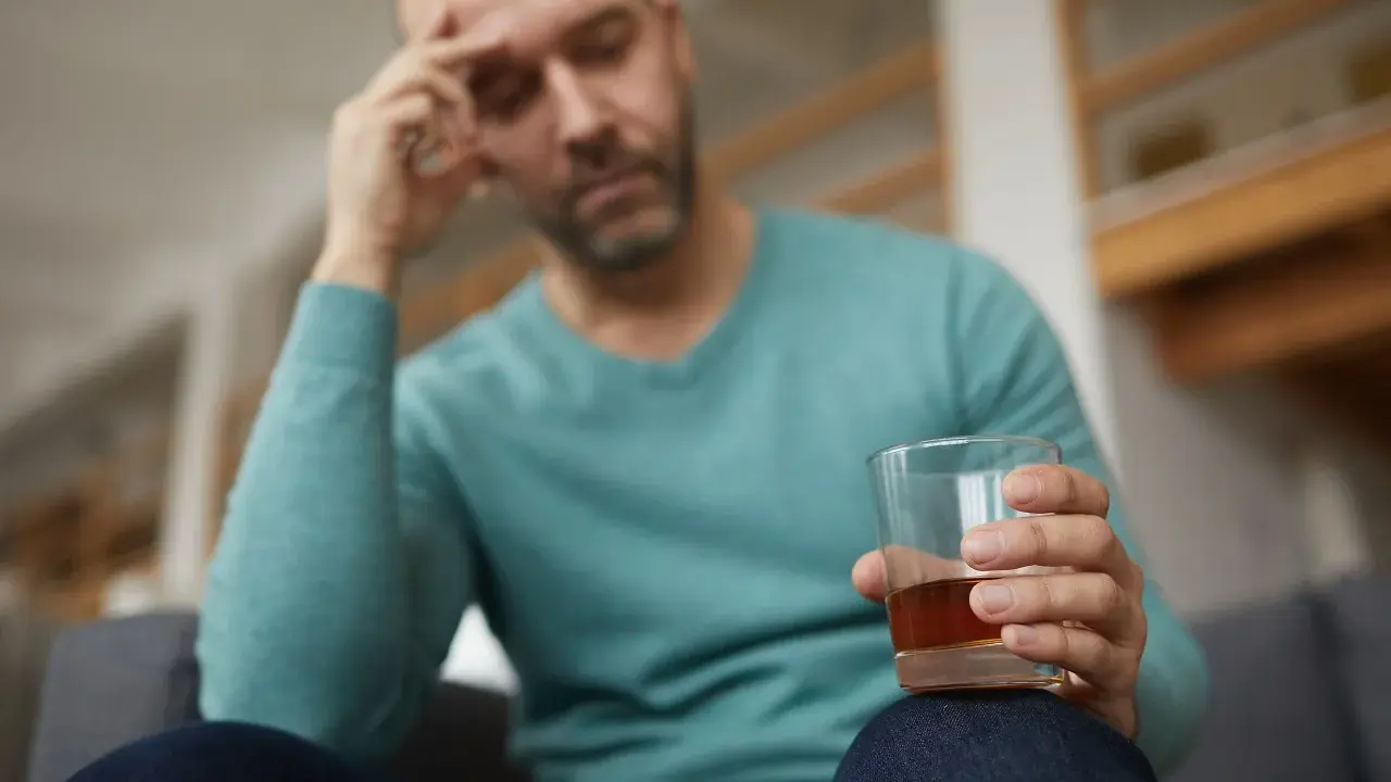 Mężczyzna z bólem głowy trzyma szklankę alkoholu, być może doświadczając reakcji disulfiramowej objawy.