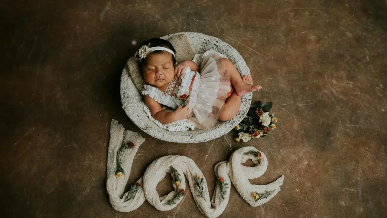 Dolce foto neonato 1 mese dorme in una cesta, circondato da fiori e dalla parola "love" creata con tessuto.