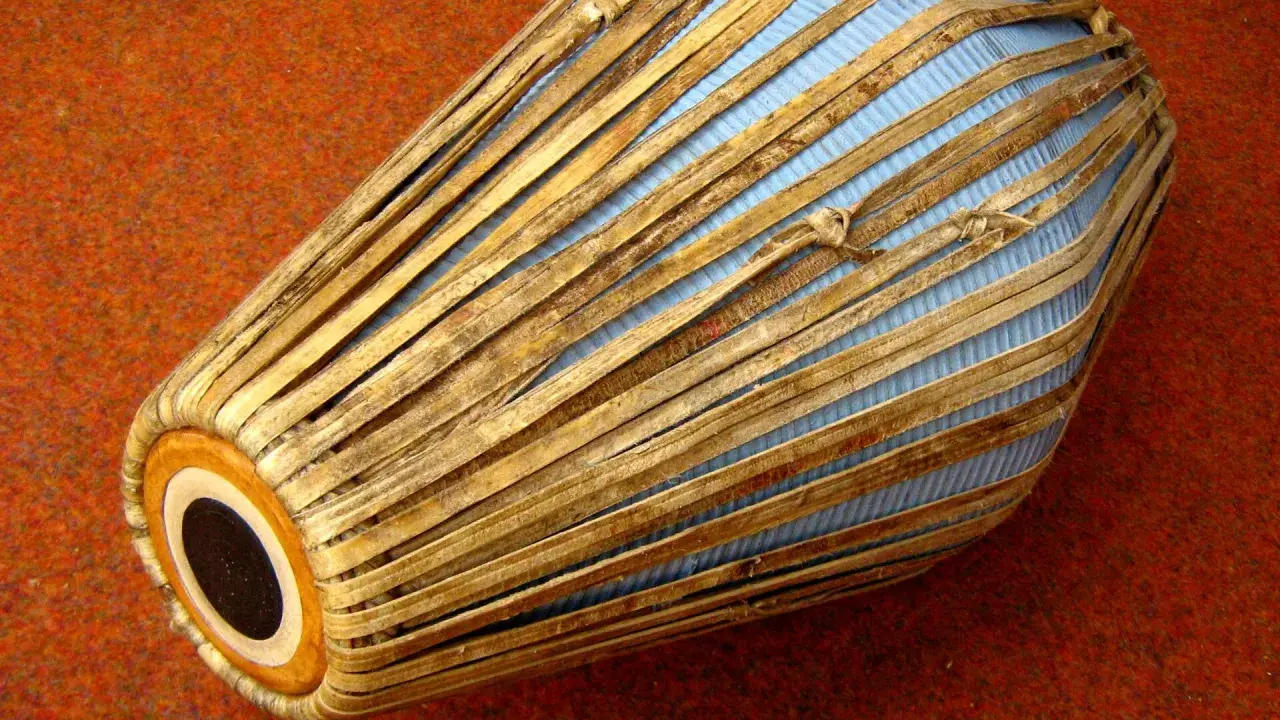 Mridanga, jeden z najstarszych instrumentów muzycznych, z niebieską membraną i drewnianymi wzmocnieniami, leży na pomarańczowym tle.