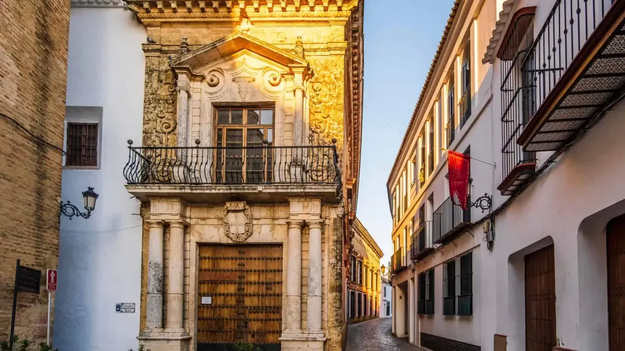Calle empedrada flanqueada por edificios históricos, un ejemplo de los pueblos bonitos de Sevilla. Fachada de piedra dorada con balcón y puerta de madera.