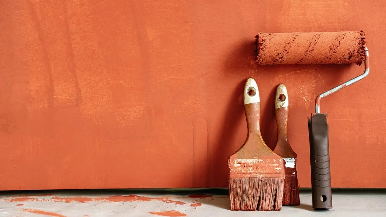 Deux pinceaux et un rouleau à peinture, prêts à rattraper trace de rouleau peinture sur un mur orange texturé.
