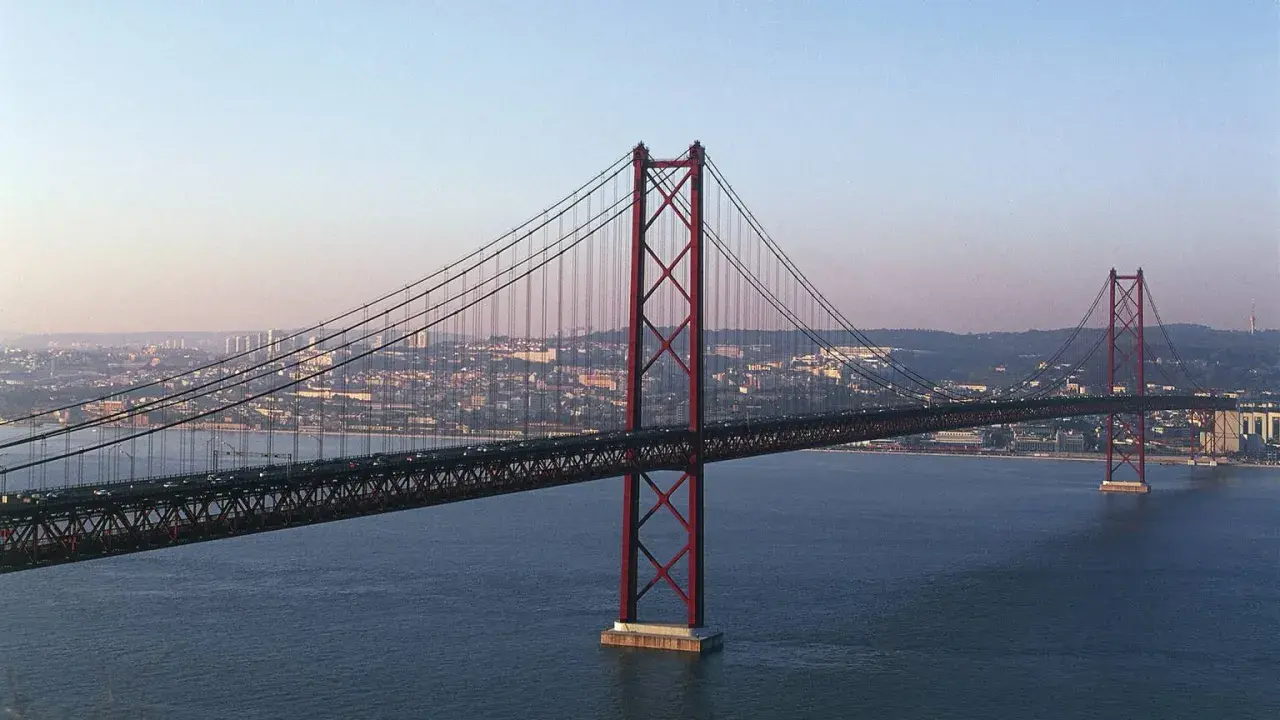 Der rote Hängebrücken-Gigant, oft als "Golden Gate Lissabon" bezeichnet, überspannt das ruhige Wasser mit der Stadt im Hintergrund.