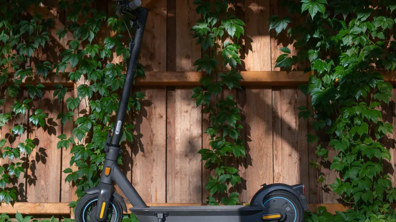 Trottinette électrique noire, prête à l'aventure, avec une puissance impressionnante, posée devant un mur de bois couvert de végétation.