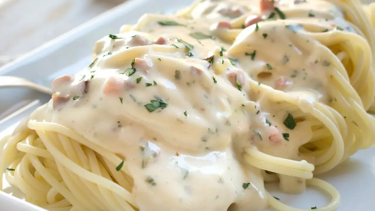 Cremige Spaghetti Carbonara mit Sahne, Speckwürfeln und Petersilie auf einem weißen Teller.