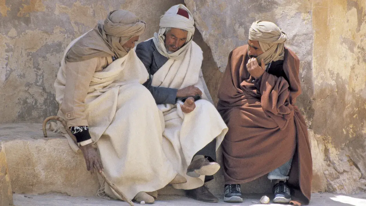 Drei Männer in traditioneller Kleidung sitzen und unterhalten sich. Sie diskutieren vielleicht, was haben Araber erfunden, während sie die Sonne genießen.