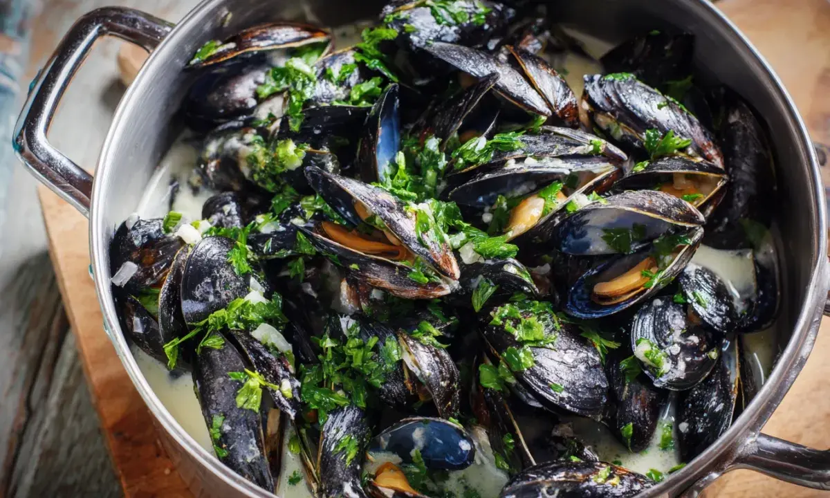 En stor gryta med ångande moules marinières, toppad med färsk persilja och serverad i en krämig vitvinssås.
