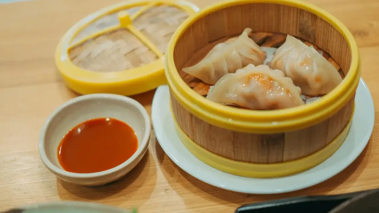 Parujące pierogi gyoza w bambusowym parowniku, obok miseczka z sosem.