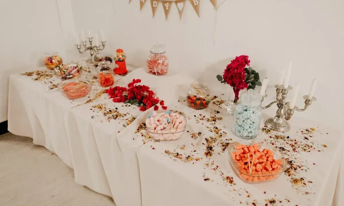 Elegante candy bar boda con dulces de colores, flores rojas y candelabros plateados.