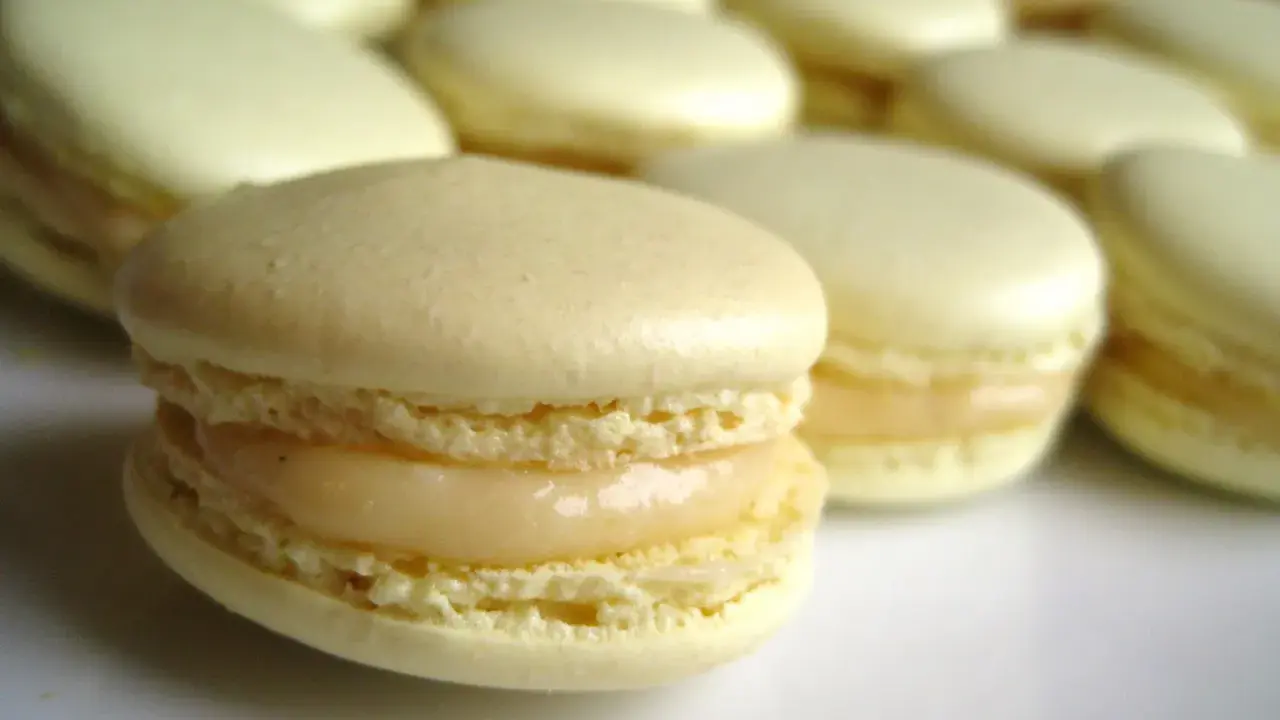 Un délicieux macaron meringue française, à la garniture crémeuse, se tient au premier plan, entouré d'autres macarons pâles.