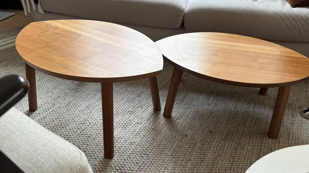 Två ovala soffbord i trä, liknande IKEA:s soffbord i Stockholm, står på en matta framför en soffa.