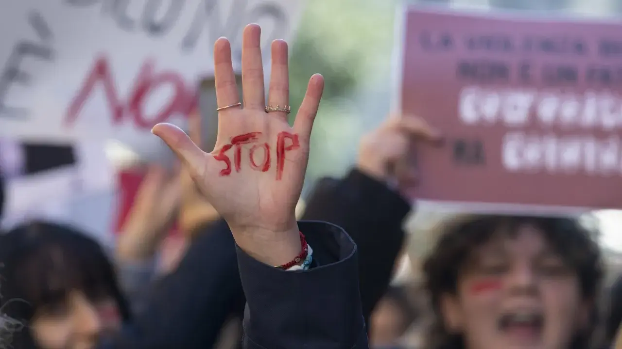 Mano alzata con "STOP" scritto in rosso, simbolo di protesta. Si evoca la necessità di una **codice rosso procedura** per proteggere le vittime.