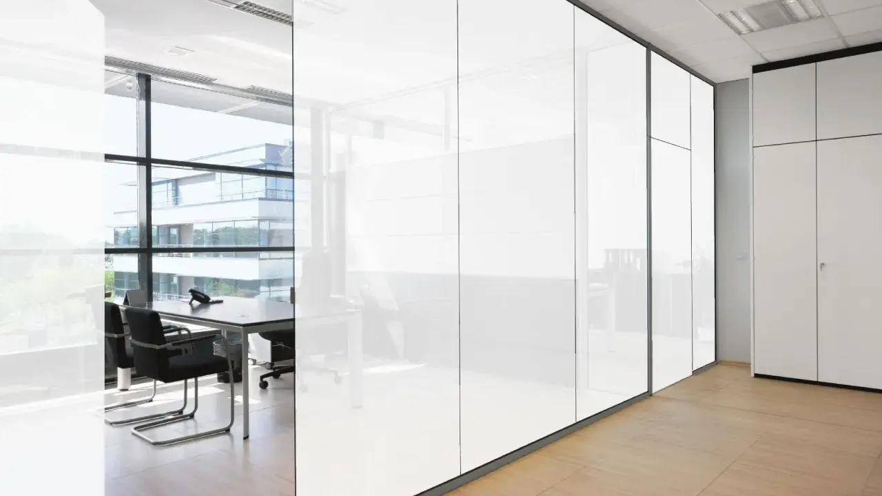 Oficina moderna con paredes de cristal que se oscurece, reflejando un edificio exterior y mobiliario de oficina.