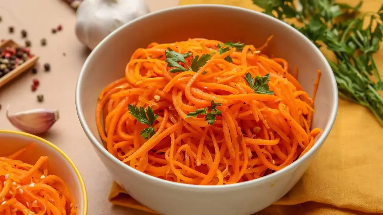 Aksamitna marchewka po koreańsku, udekorowana natką pietruszki, obok czosnku i kolorowego pieprzu.