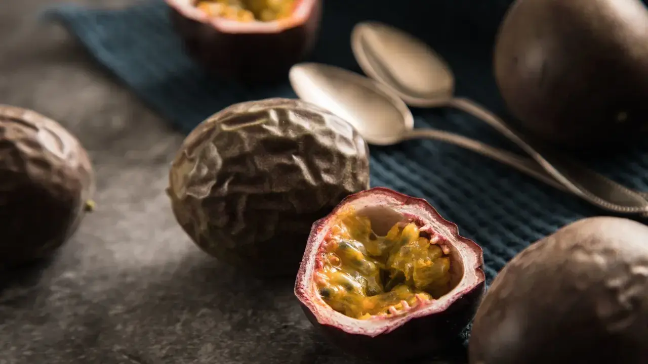 Reife Passionsfrüchte, eine aufgeschnitten, zeigen ihr saftiges Inneres. Zwei Löffel liegen bereit, um die exotische Frucht zu genießen.