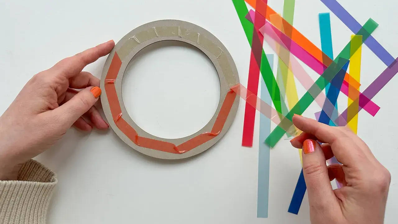 Hände bereiten einen Ring für Fenstersterne vor, indem sie bunte Streifen zum Falten bereitlegen.
