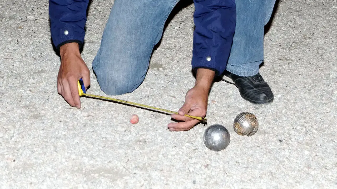 Un joueur de pétanque mesure la distance entre les boules. On se demande combien gagne un joueur de pétanque professionnel.