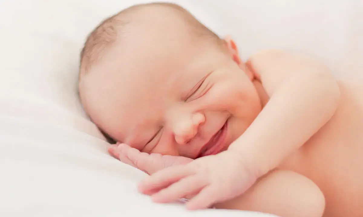 Un bebé duerme plácidamente, con una sonrisa que nos hace preguntar porque sonrien los bebes. Su carita refleja paz y felicidad.