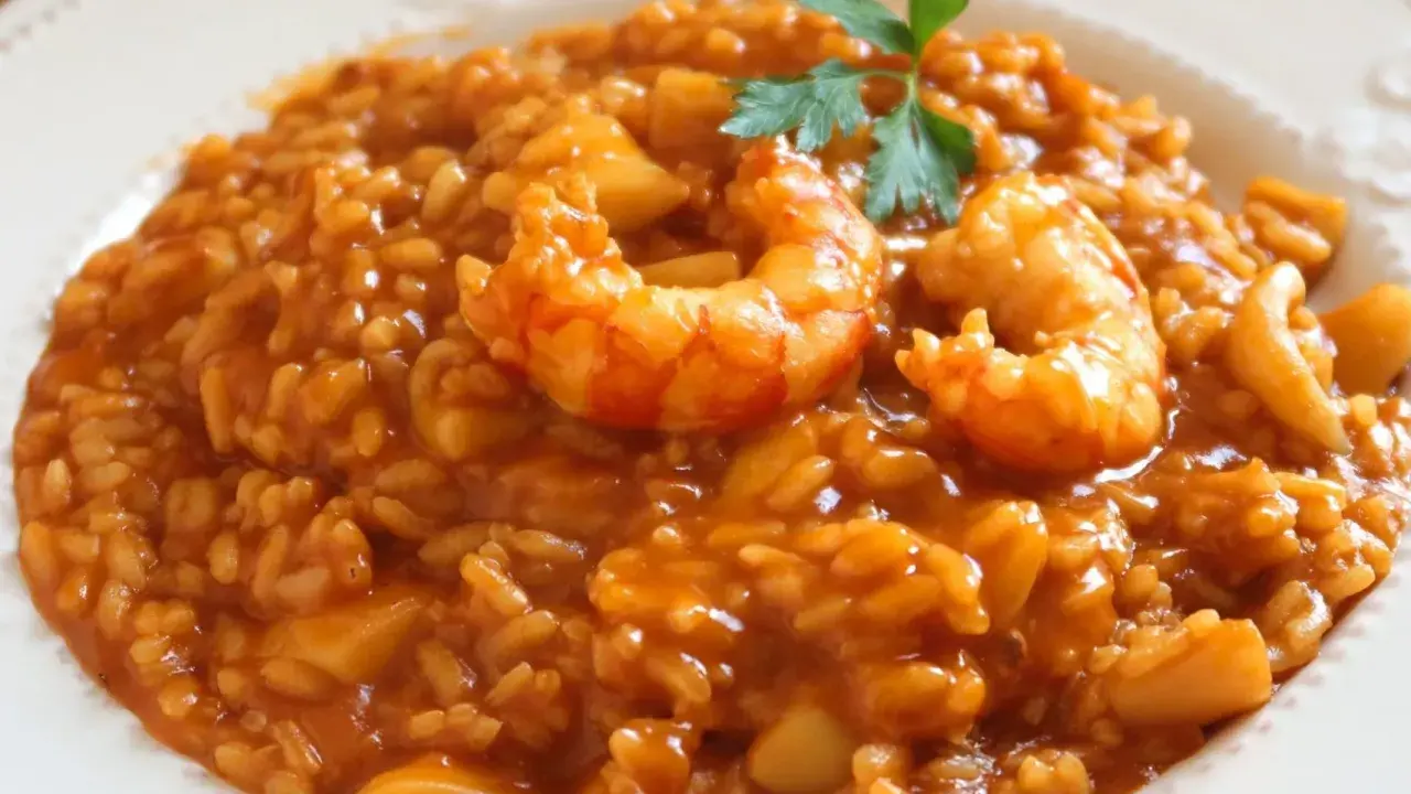 Delicioso arroz caldoso con gambas y trozos de calamar, adornado con una ramita de perejil.