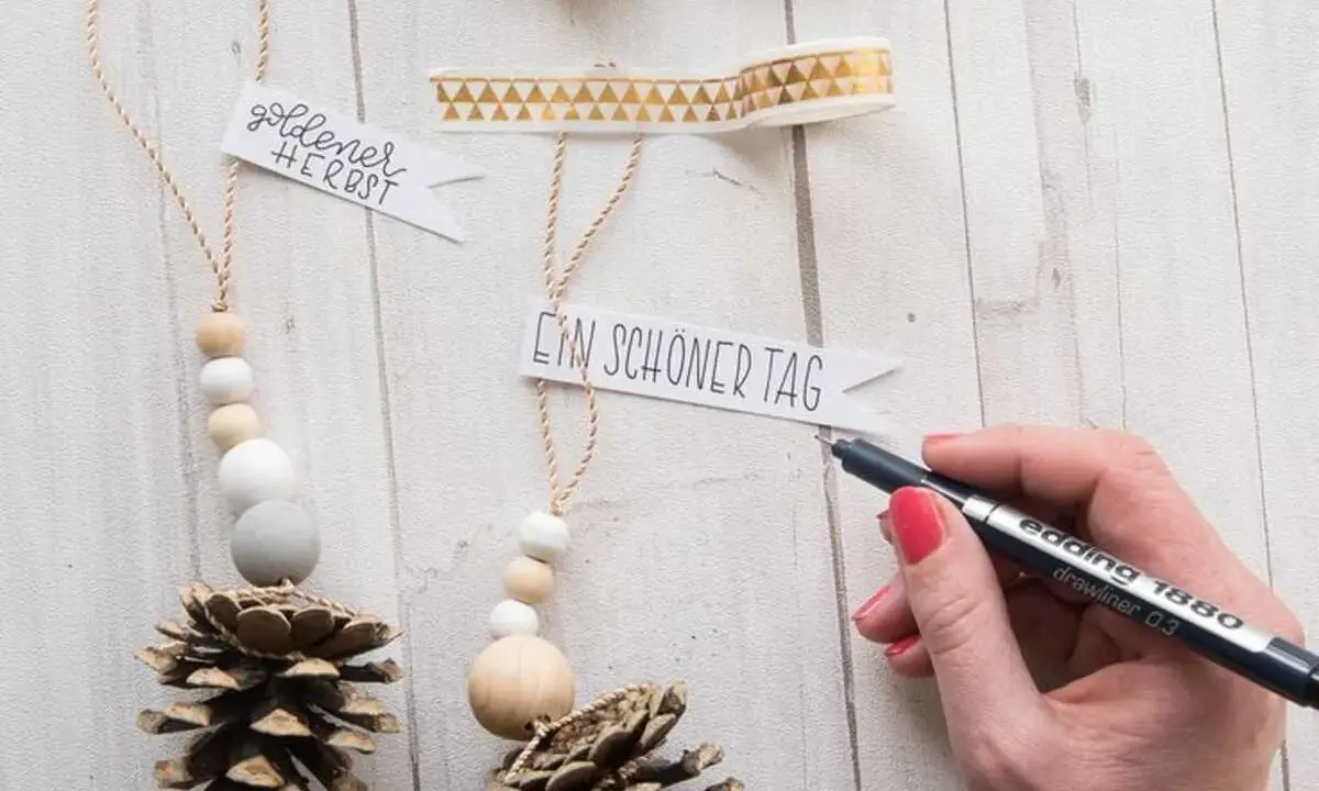 Déco Noël pomme de pin à faire soi-même : des suspensions naturelles avec perles en bois et messages personnalisés.