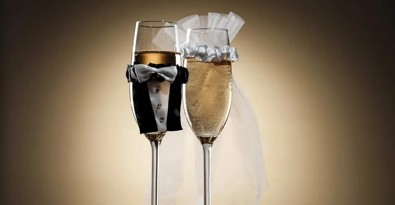 Dwa kieliszki szampana, jeden w stroju pana młodego, drugi z welonem panny młodej. Idealne wino dla pary młodej na toast.