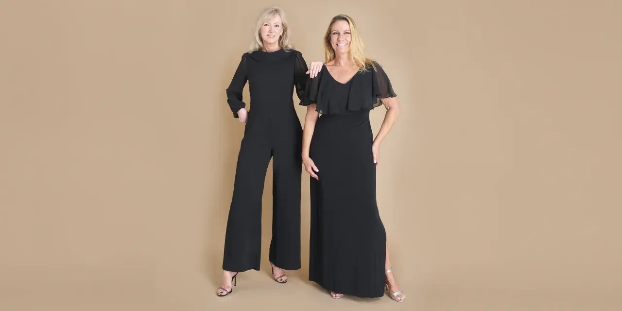 Two women in elegant black evening attire, a wide-leg jumpsuit and a flowing gown, ready for a formal event.