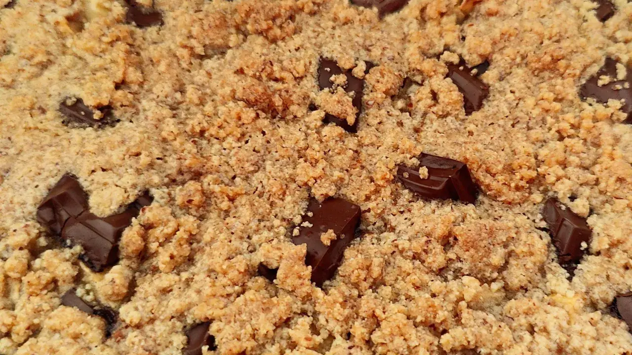 Gros plan sur un délicieux crumble pomme amande parsemé de morceaux de chocolat noir fondants.