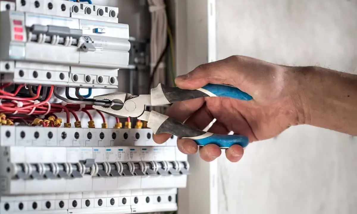 Elektryk pracuje przy skrzynce z bezpiecznikami. Gdy zgłosić brak prądu, warto sprawdzić właśnie takie instalacje.