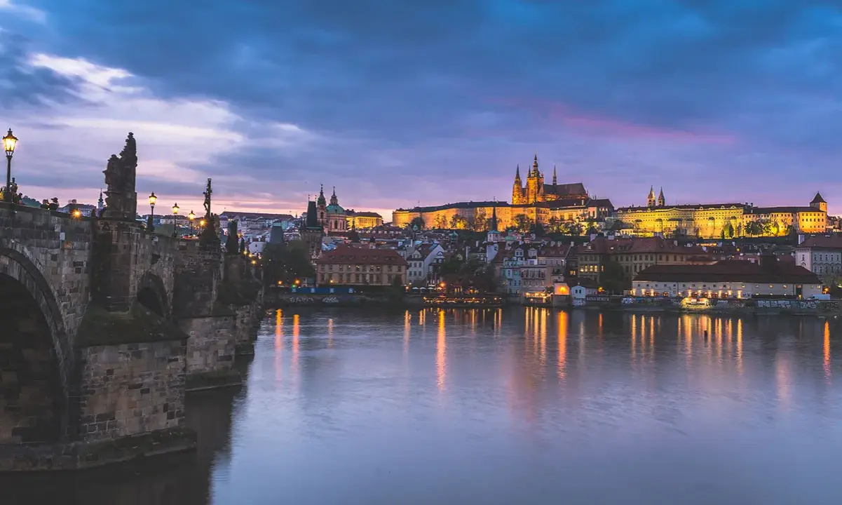 Nastrojowa fotografia nocna Pragi: Most Karola i Zamek na Hradczanach w blasku świateł, odbijających się w Wełtawie.