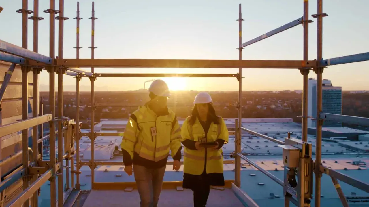 Två byggarbetare i varselkläder inspekterar ett bygge vid solnedgången. De diskuterar säkerhetslösningar, som brandklass EI60.