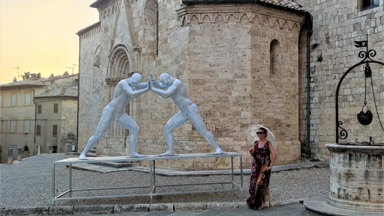 Sculture di due uomini che si spingono a San Quirico d'Orcia, con una donna con ombrellino.