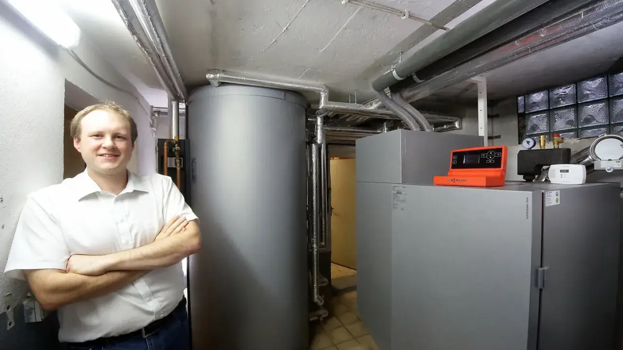 Mann vor Pelletheizung und großem Speicher in Heizungsraum.