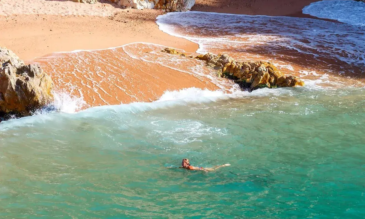 Eine Frau schwimmt im türkisfarbenen Meer vor einer sandigen Bucht in Palamós, Spanien.