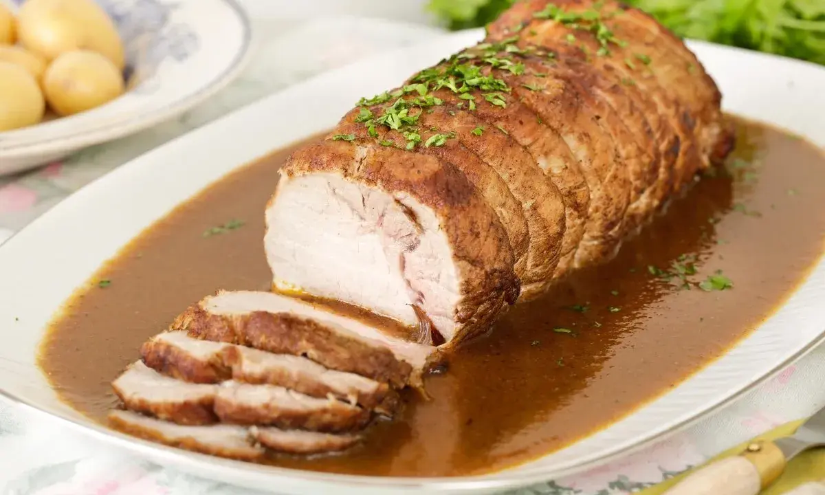 Lomo de cerdo al horno en papel aluminio, jugoso y tierno, bañado en salsa y espolvoreado con perejil.